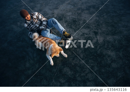 Dark ice, top view. Man with Akita Inu dog is on the ice with skates in winter 135643116
