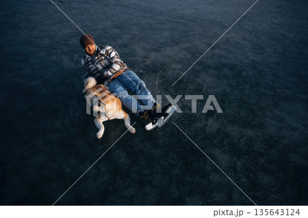 View from the top, lying down. Man with Akita Inu dog is on the ice with skates in winter View from the top, lying down. Man with Akita Inu dog is on the ice with skates in winter 135643124