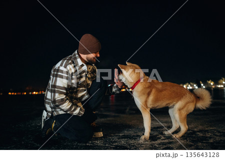 Training the tricks, giving paw. Man with Akita Inu dog is on the ice with skates in winter Training the tricks, giving paw. Man with Akita Inu dog is on the ice with skates in winter 135643128