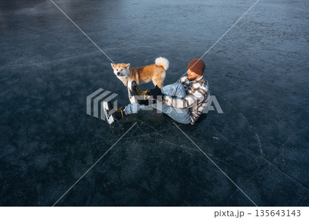 Be ready, preparing for the ride. Man with Akita Inu dog is on the ice with skates in winter Be ready, preparing for the ride. Man with Akita Inu dog is on the ice with skates in winter 135643143