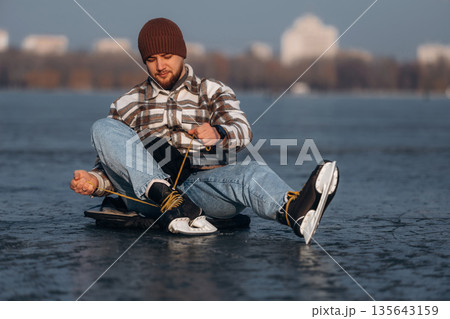 Getting ready, wearing skates. A man is on the ice in winter Getting ready, wearing skates. A man is on the ice in winter 135643159