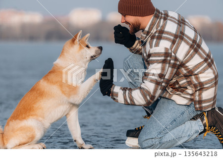 Learning the tricks, giving a paw. Man with Akita Inu dog is on the ice with skates in winter 135643218