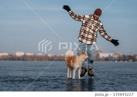 Outdoors together. Man with Akita Inu dog is on the ice with skates in winter Outdoors together. Man with Akita Inu dog is on the ice with skates in winter 135643227