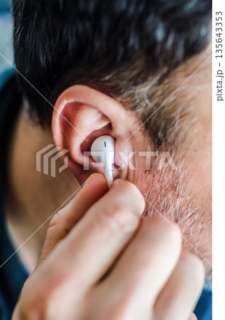 Tuning In: Close-Up of a Man Placing an Earbud in His Ear. Tuning In: Close-Up of a Man Placing an Earbud in His Ear. 135643353
