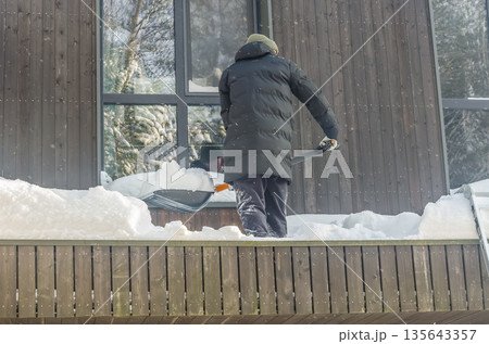 Man Shoveling Deep Snow From a Modern House Balcony. Man Shoveling Deep Snow From a Modern House Balcony. 135643357