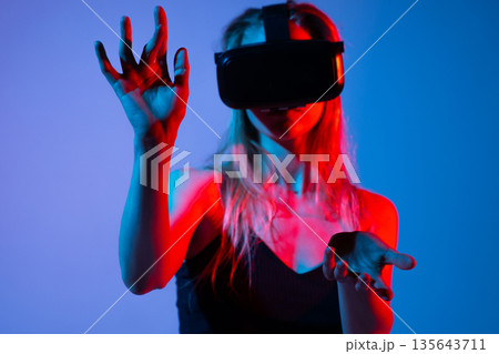 Close up of woman interacting with virtual interface using hands and VR headset, immersive futuristic technology concept with neon lighting 135643711