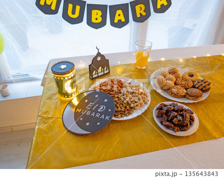 Eid Mubarak table with Ramadan sweets, dates, nuts and festive decor 135643843