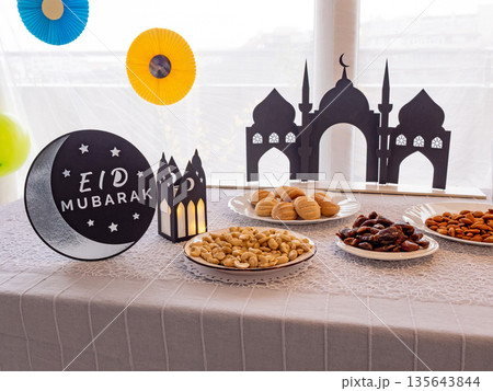 Eid Mubarak table with Ramadan sweets, dates, nuts and festive decor 135643844