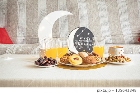 Eid Mubarak table with Ramadan sweets, dates, nuts and festive decor 135643849