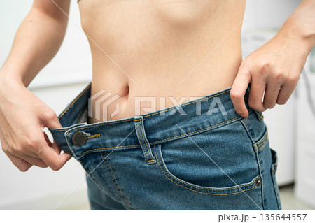Young Asian woman losing weight wearing loose pants in oversize jeans. 135644557