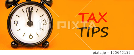 Tax tips symbol. Concept word Tax tips on beautiful orange paper. Beautiful black alarm clock. Beautiful orange paper background. Business tax tips concept. Copy space. Tax tips symbol. Concept word Tax tips on beautiful orange paper. Beautiful black alarm clock. Beautiful orange paper background. Business tax tips concept. Copy space. 135645155