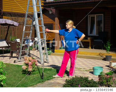 Mature woman outdoor with ladder. Senior woman doing home repair work on house. Renovation or DIY concept. Housewife at home. 135645546