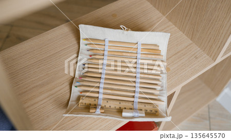 Natural wooden colored pencils and ruler in fabric pouch on wooden shelf Natural wooden colored pencils and ruler in fabric pouch on wooden shelf 135645570