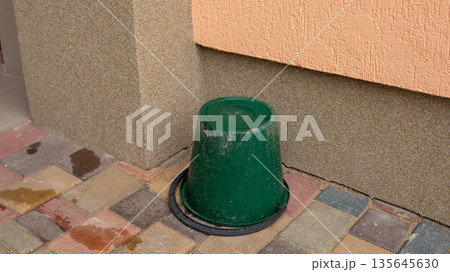 Upside-down green bucket on colorful tiled ground near wall Upside-down green bucket on colorful tiled ground near wall 135645630