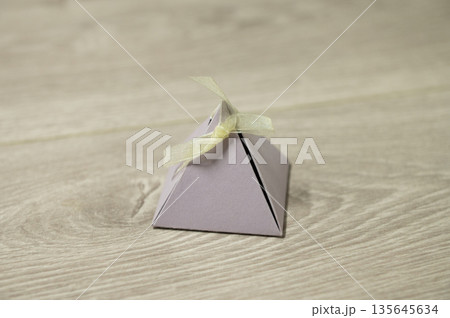 Small grey pyramid gift box with ribbon on wooden surface Small grey pyramid gift box with ribbon on wooden surface 135645634