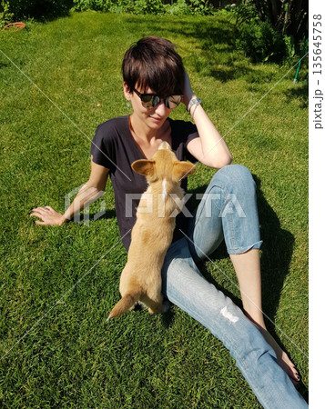 Happy Woman Holding Corgi Puppy in Sunny Garden 135645758