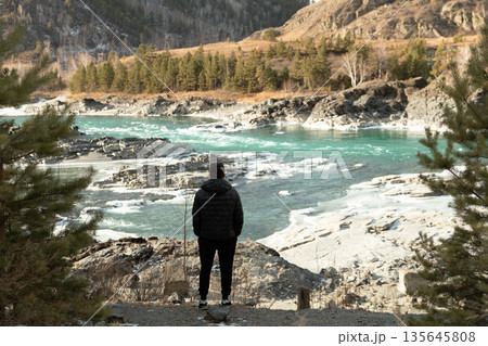 Man Observing Icy Turquoise River in Winter Mountain Landscape Man Observing Icy Turquoise River in Winter Mountain Landscape 135645808