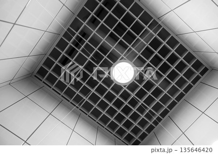 A monochrome interior shot of a tiled ceiling with a light A monochrome interior shot of a tiled ceiling with a light 135646420