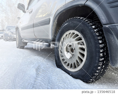 Deflated car wheel. Car is in parking lot. A broken wheel at the car in the cold, in winter. Close up photo 135646518