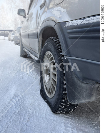 Deflated car wheel. Car is in parking lot. A broken wheel at the car in the cold, in winter. Close up vertical photo 135646909