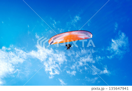 Silhouette of a paraglider flying a powered parachute (paramotor). 135647941
