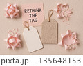 Rethink tag message with pink paper flower, piggy bank, notebook, and scattered origami decorations on neutral background representing sustainable gift wrapping concept 135648153