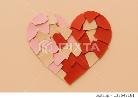 Broken heart shape crafted from red and pink paper piece arranged on beige background representing relationship breakup and heartbreak emotion for valentine day 135648161