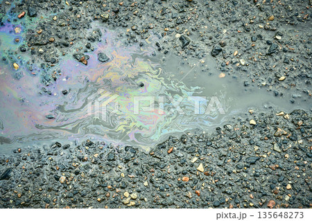 Oil slick creating a colorful rainbow pattern in a puddle on rough asphalt. 135648273