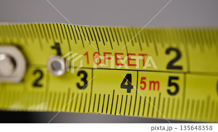 Macro view of a metal retractable tape measure showing feet and metric increments 135648358