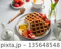 Belgian waffles with strawberries and honey, cup of tea and fresh fruits. Homemade breakfast table setting with tulip flower bouquet 135648548