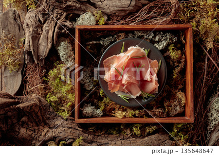 Prosciutto with rosemary on a black plate in abstract natural composition. 135648647
