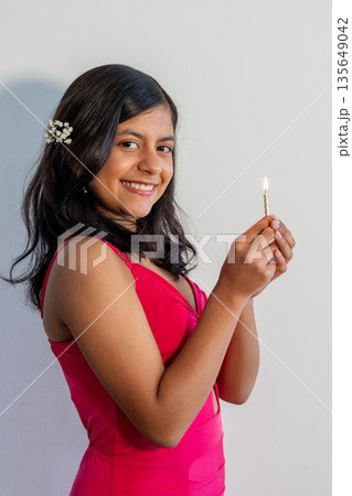 A teen in a red dress is holding a lit candle A teen in a red dress is holding a lit candle 135649042