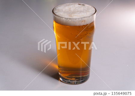 Full pint glass of golden lager beer with frothy foam head. Vertical studio shot of amber ale on white background with copy space Full pint glass of golden lager beer with frothy foam head. Vertical studio shot of amber ale on white background with copy space 135649075