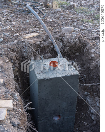 Concrete foundation block with anchor bolts and orange PVC pipe in a trench. Construction site infrastructure detail Concrete foundation block with anchor bolts and orange PVC pipe in a trench. Construction site infrastructure detail 135649079