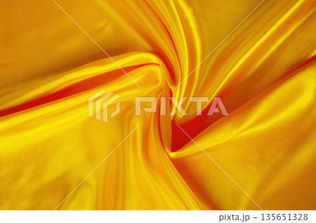 Golden silk fabric texture with dramatic swirling folds and radiant highlights for luxury abstract backgrounds. 135651328