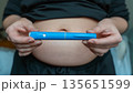 GLP-1 injection pen held by woman in front of abdomen, weight management concept 135651599