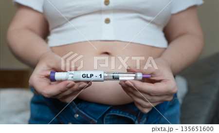 GLP-1 injection pen held by woman in front of abdomen, weight management concept 135651600