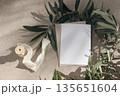 Mediterranean mock-up scene, summer birthday wedding invitations. Blank greeting card, olive branches, ribbon on beige stone background in sunlight. Floral shadows overlay. Feminine flat lay, top view 135651604