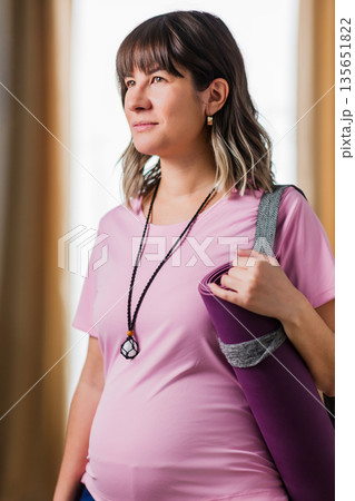 Hispanic pregnant woman looking away carrying yoga mat 135651822