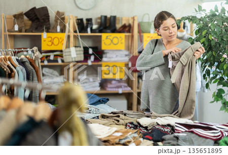 Pregnant european young female client choosing new trousers in clothing mall Pregnant european young female client choosing new trousers in clothing mall 135651895