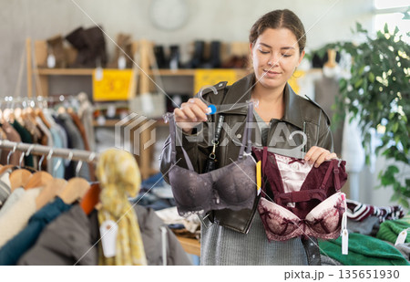 Girl is busy looking at clothes items in store, she chooses bra Girl is busy looking at clothes items in store, she chooses bra 135651930