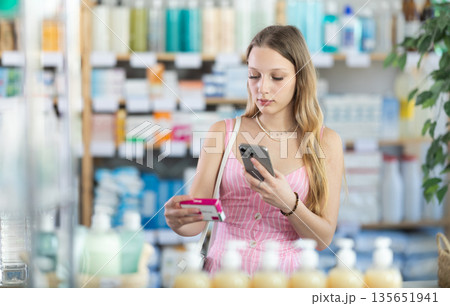 woman in a dress stands in a pharmacy and scans a package of paracetamol 135651941