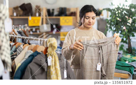 Latin girl is busy looking at clothes items in store, she chooses trousers Latin girl is busy looking at clothes items in store, she chooses trousers 135651972