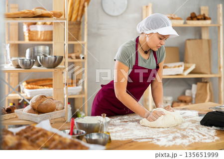 Woman works in bakery as baker, kneads dough, works with flour. 135651999