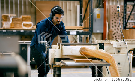 Carpenter working wood with planer machine in workshop Carpenter working wood with planer machine in workshop 135652386