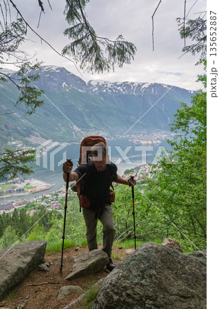 Male hiker climbing steep trail overlooking Hardangerfjord and Odda, Norway Male hiker climbing steep trail overlooking Hardangerfjord and Odda, Norway 135652887