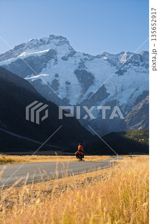 Cyclist riding past massive glaciers near Mount Cook Village, New Zealand 135652917