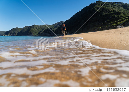 Low angle of barefoot hiker walking on beach with sea foam, Abel Tasman, NZ 135652927