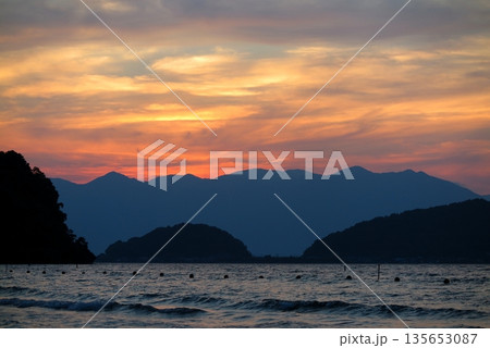 夕暮れの琵琶湖畔：近江八幡市の湖岸から眺めた沖島の一部と、遠方に比良山地のシルエット 135653087