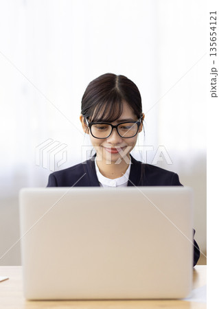 デスクでパソコン作業をするメガネをかけたスーツ姿の若い女性 135654121